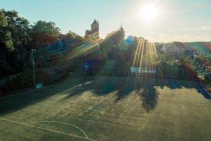 Fußballfeld mit Sicht auf eine Burg im Hintergrund, beleuchtet von der Morgensonne mit strahlenden Lichtverhältnissen.