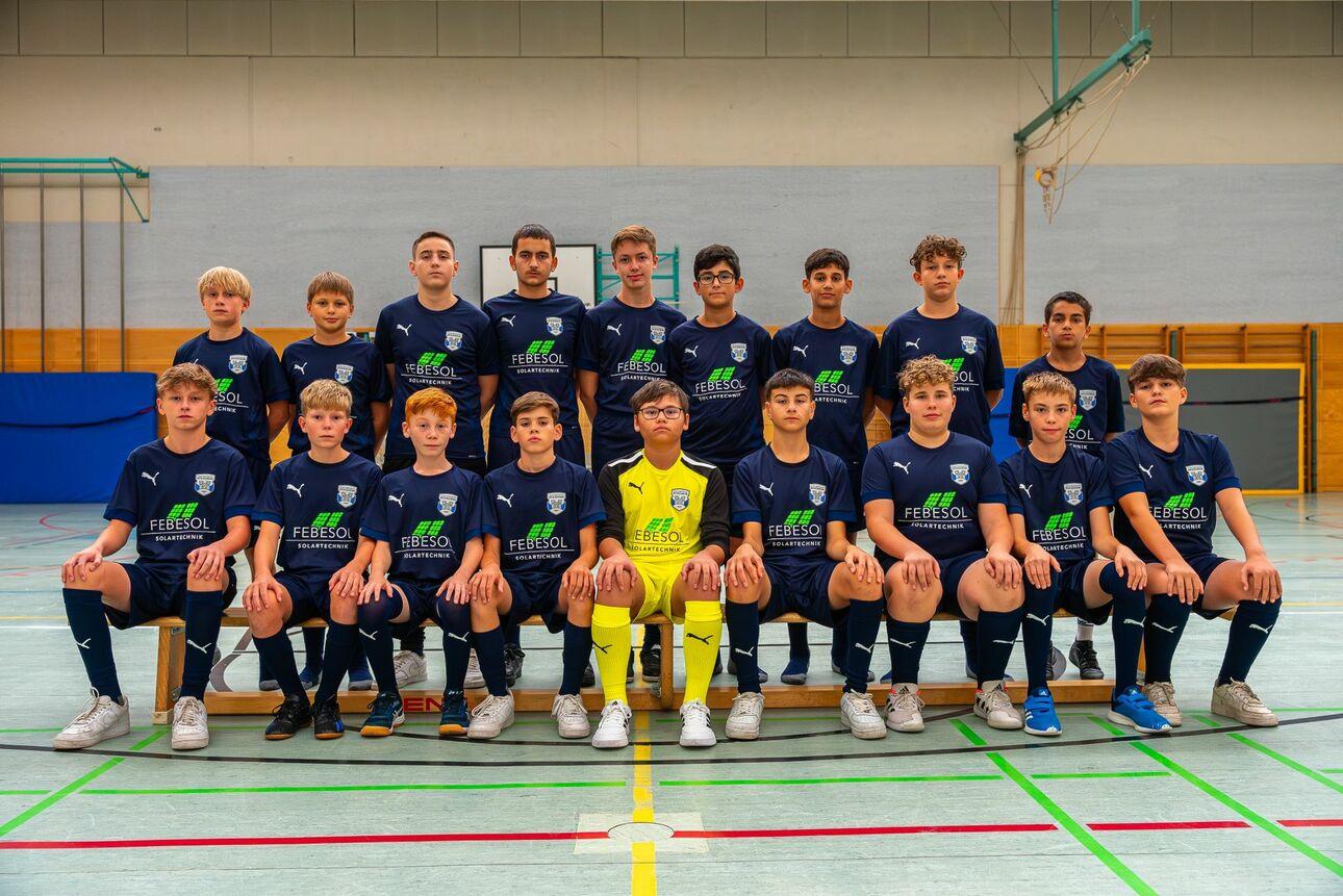 Mannschaftsfoto einer Fußballjugendgruppe, bestehend aus 15 Jungen in blauen Trikots, auf einem Hallenboden.