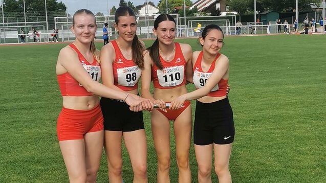 Vier Mädchen in Sportkleidung stehen auf einem grünen Rasen und halten sich an den Händen.