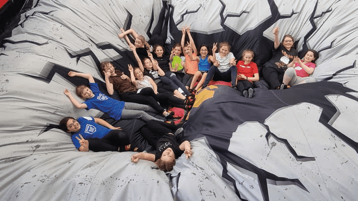 Gruppe von Kindern liegt auf einer großen, elastischen Matte mit Riss-Muster und posiert fröhlich für die Kamera.