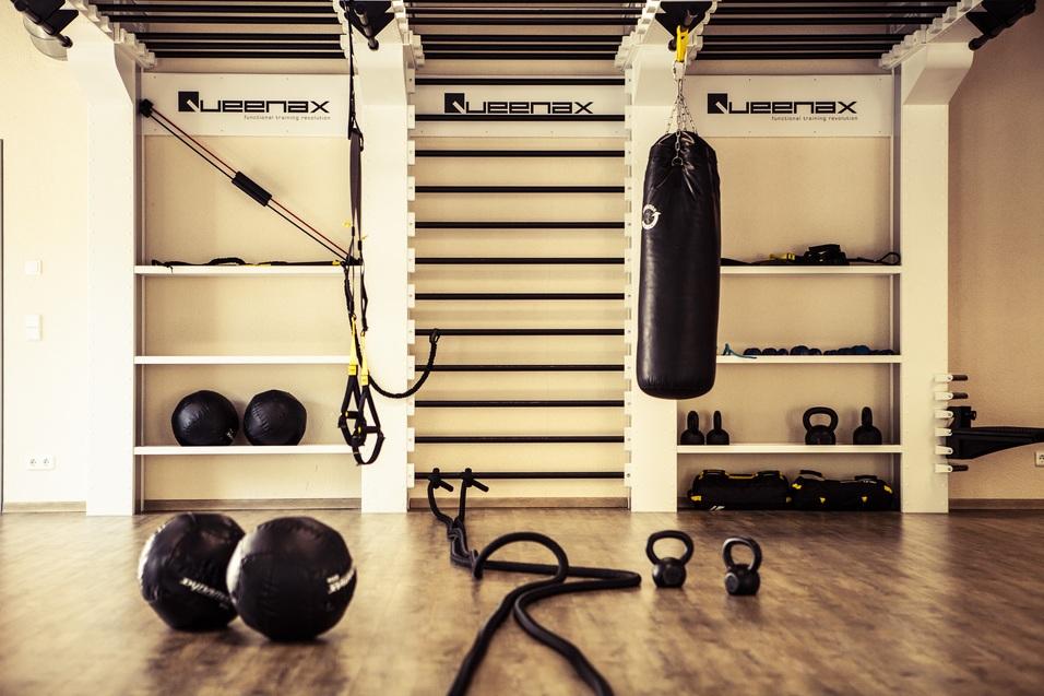 Fitnessraum mit einem Sandsack, Kettlebells, Matzentrainern und Trainingsgeräten auf Regalen vor Holzfußboden.