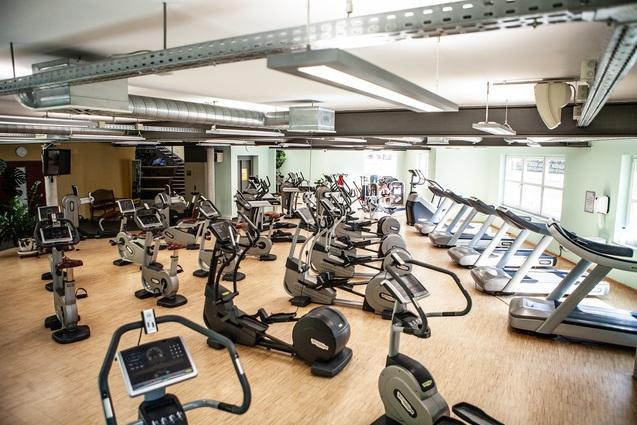 Fitnessraum mit verschiedenen Cardio-Geräten, darunter Laufbänder und Fahrräder, auf einem Holzboden.