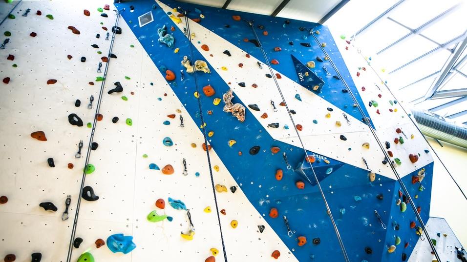 Blick auf eine Kletterwand mit bunten Griffen und Sicherungselementen in einer Indoor-Kletterhalle.