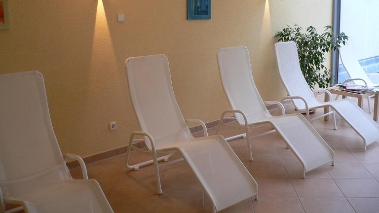 Ruhebereich mit fünf weißen Liegen, sanft beleuchtet, einer Pflanze und Fensterelementen.