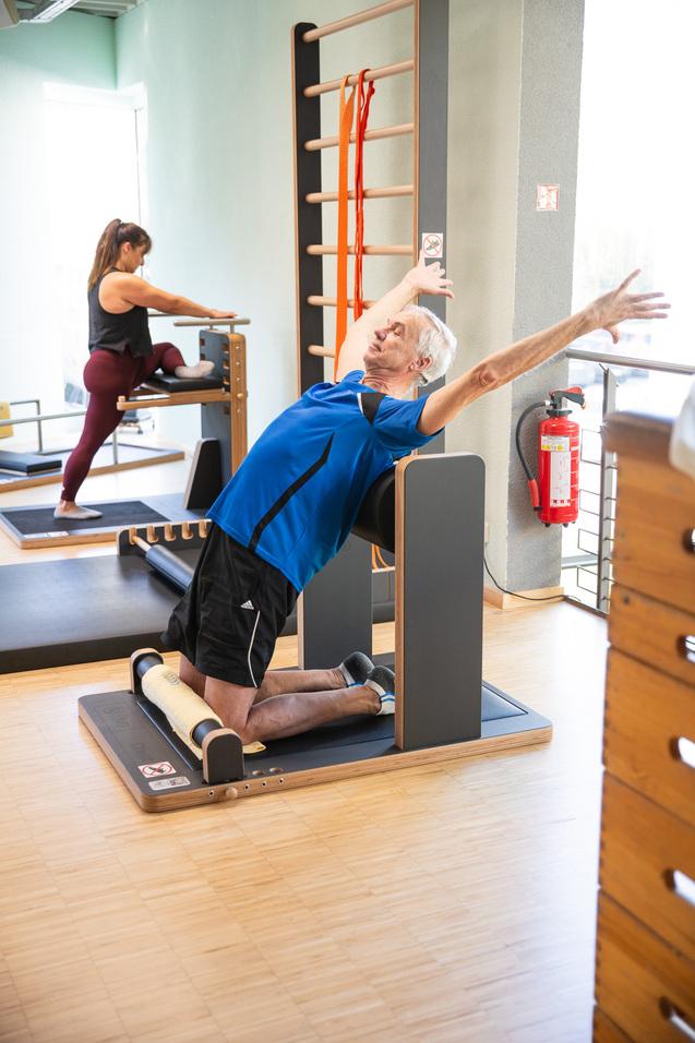 Zwei Personen in einem Fitnessraum, eine dehnt im Hintergrund, ein Mann streckt sich auf einer Fitnessbank.