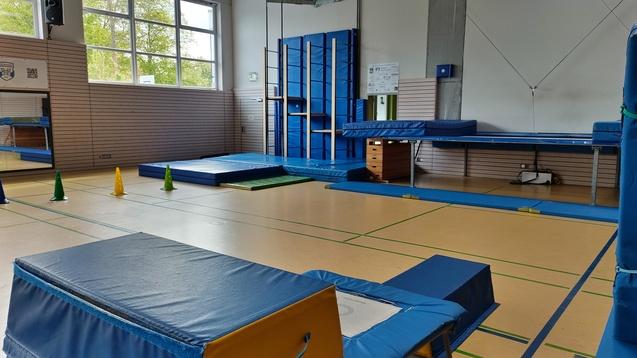 Turnhalle mit blauen Turngeräten, Matten und ausreichend Platz für Aktivitäten sowie farbigen Kegeln auf dem Boden.