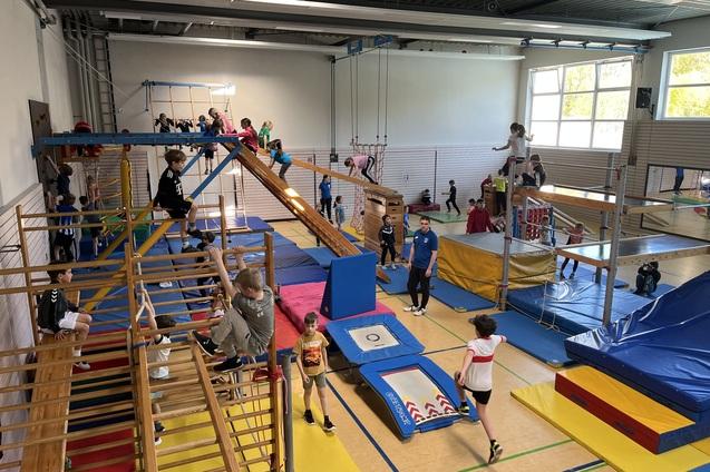 verschiedene Geräte in der Sporthalle sind aufgebaut. Kinder toben darauf