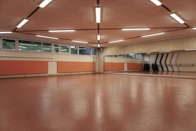 Großer, leerer Tanzraum mit orangefarbenen Wänden, Spiegeln und einem hellen, glatten Boden.
