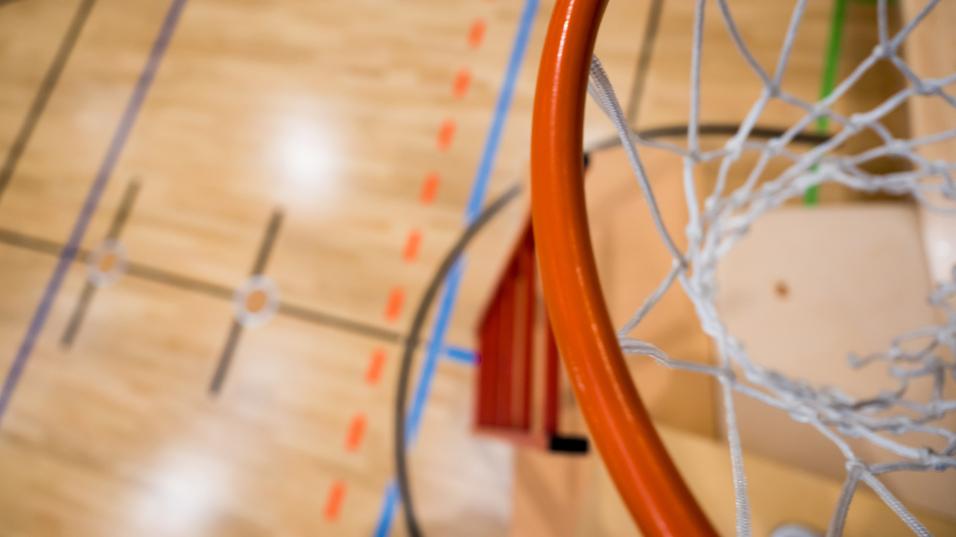 Nahaufnahme eines Basketballkorbs mit Netz über einem aufgezeichneten Basketballfeld aus Holz.