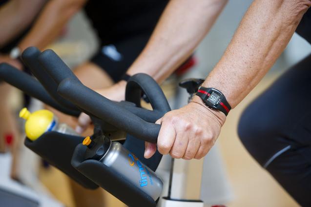 Nahaufnahme von Händen, die an den Lenkern eines Spin- und Getränkeflaschenhalter eines Fitnessbikes greifen.