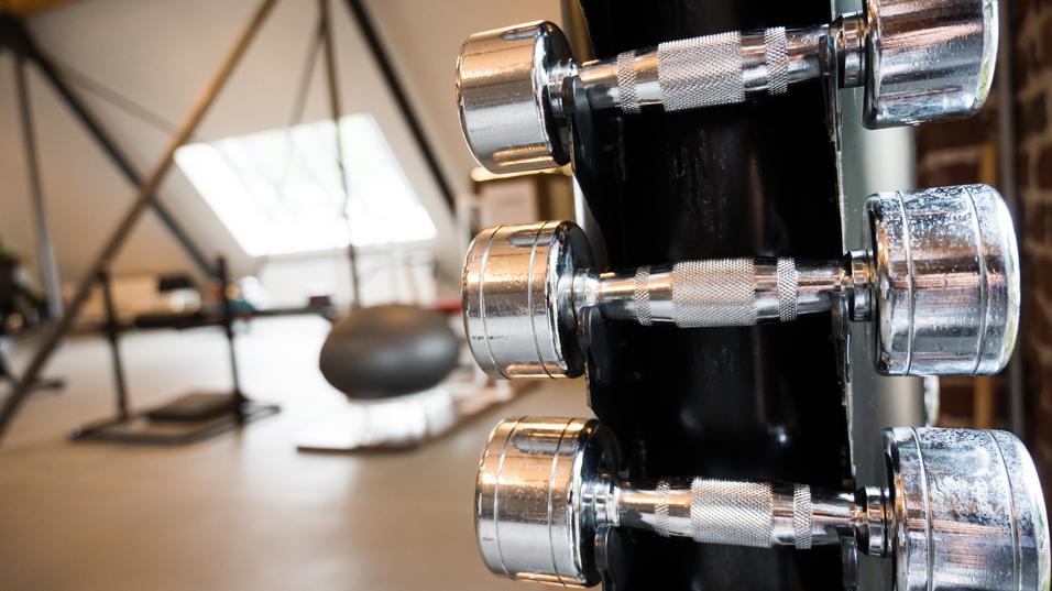 Nahaufnahme von mehreren chromierten Hanteln an einem Ständer in einem modernen Fitnessstudio.