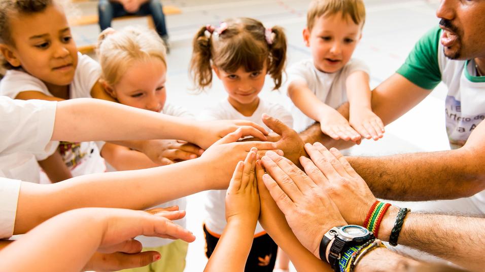 Kinder und Erwachsene legen ihre Hände in einem Kreis zusammen, symbolisieren Zusammenarbeit und Gemeinschaft.
