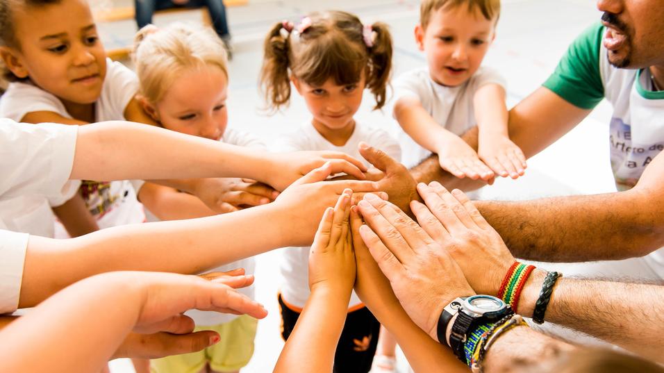Kinder und Erwachsene legen ihre Hände in einem Kreis zusammen, symbolisieren Zusammenarbeit und Gemeinschaft.
