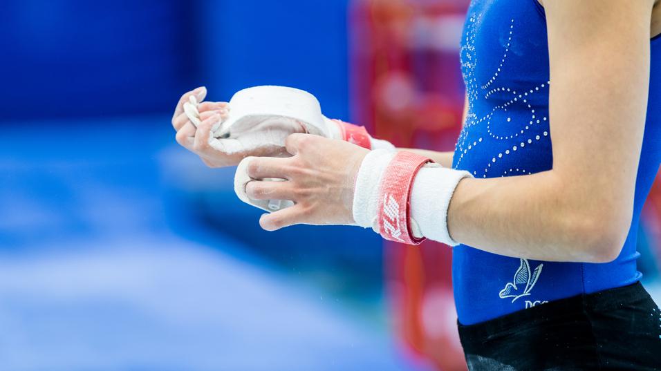 Nahaufnahme einer Sportlerin mit Kreide in der Hand, die ihre Hände mit einem roten Handgelenkschutz umwickelt.